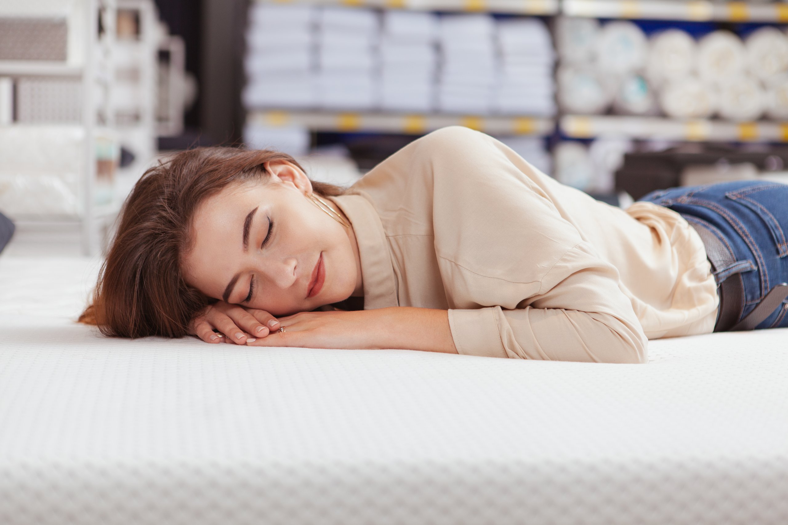 Young beautiful woman smiling with her eyes closed, lying on orthopedic mattress at furniture store